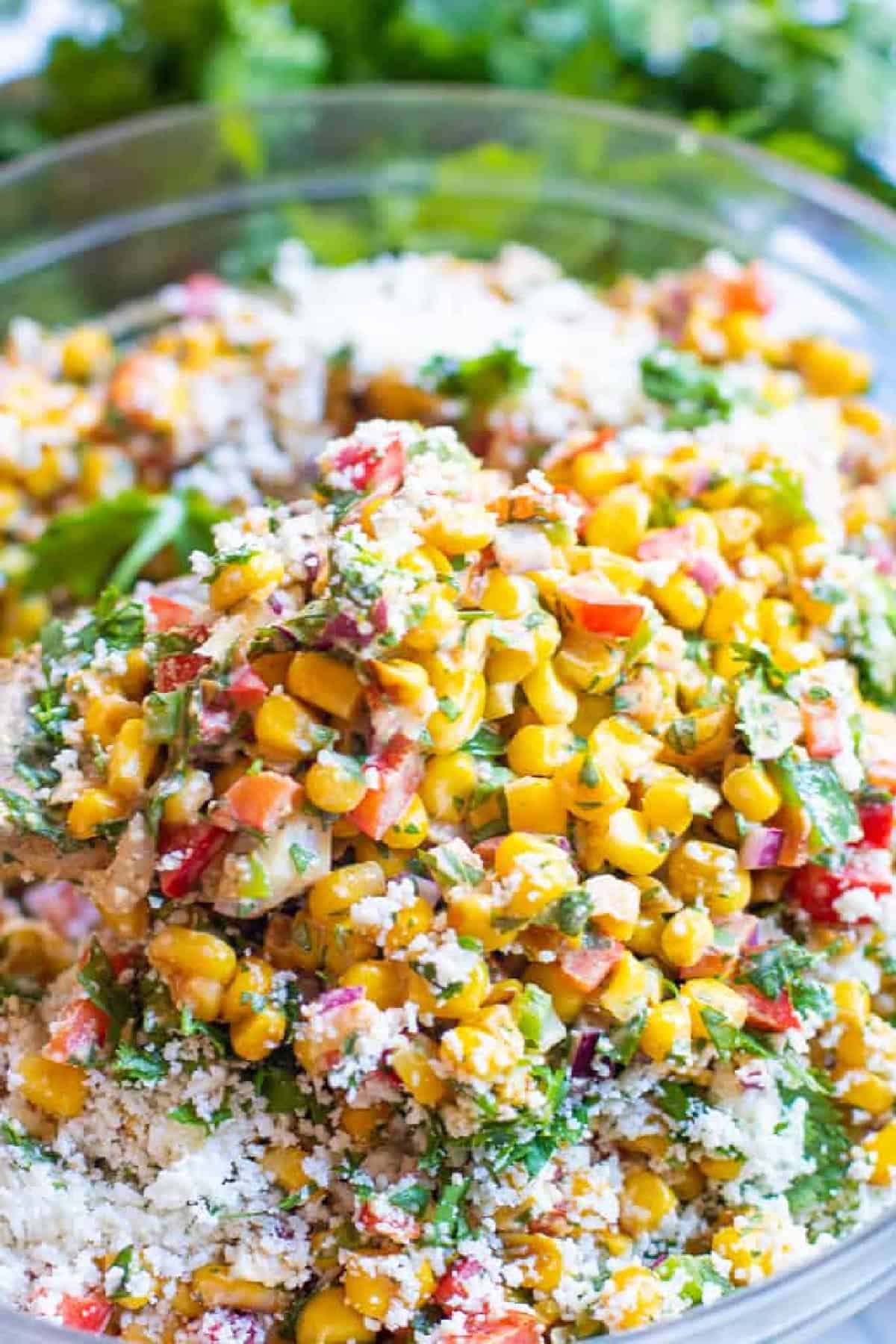 a bowl of mexican street corn salad with a spoon picking up a big spoonful of it.