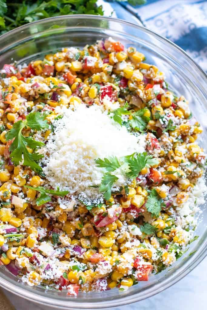 a bowl of corn salad with red pepper, cilantro, and shredded cheese.