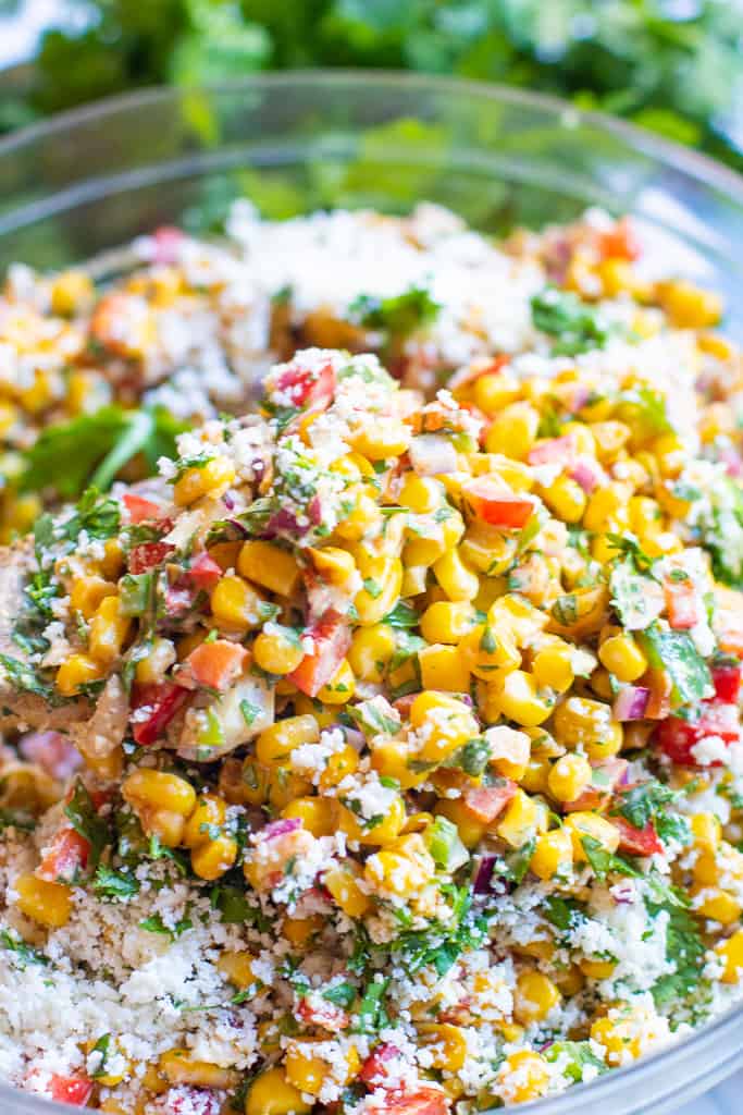 a bowl of corn salad with red pepper, cilantro, and shredded cheese.