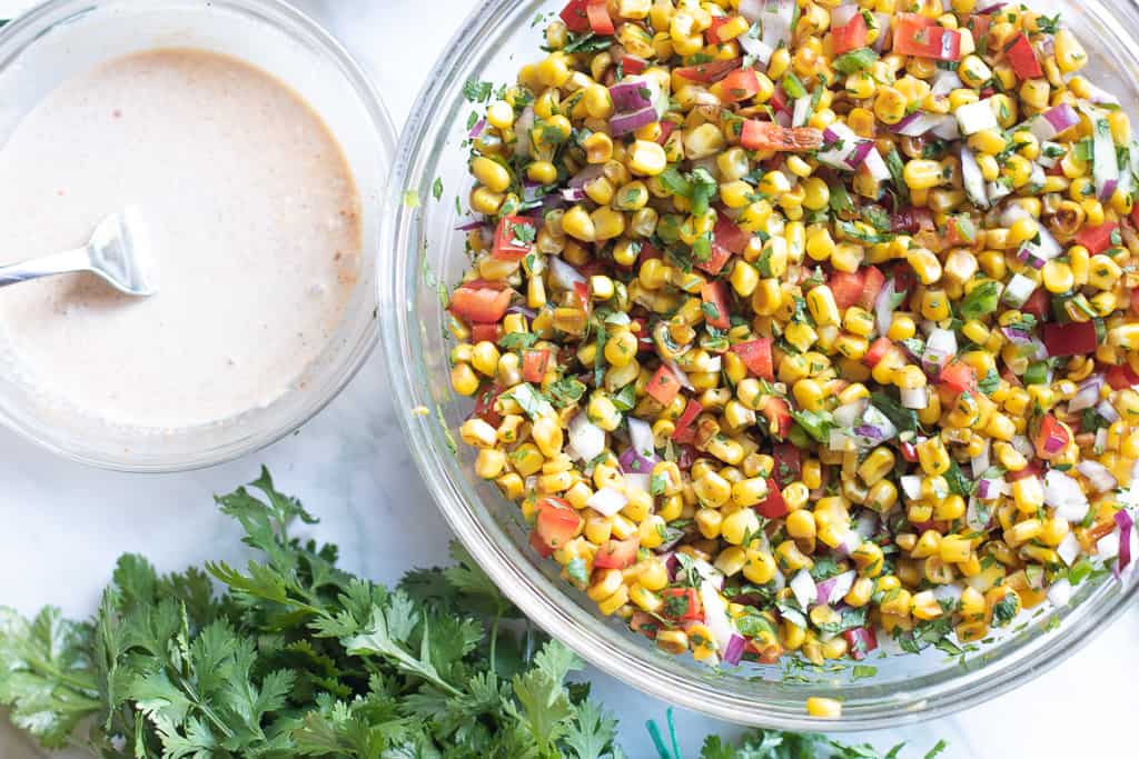 Mexican street corn salad dressing in a bowl next to mixed veggies.