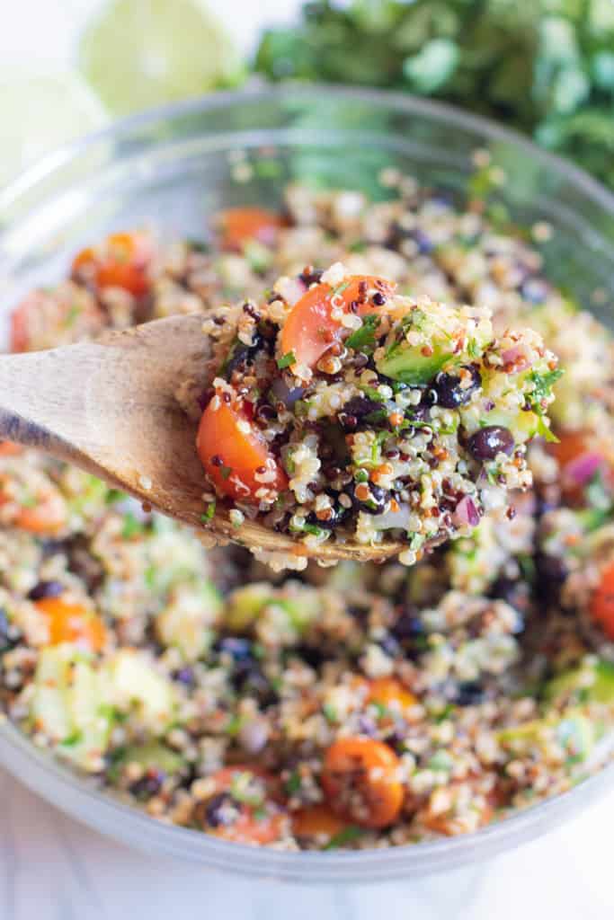 a bowl of quinoa salad with a close up of a wooden spoon of it