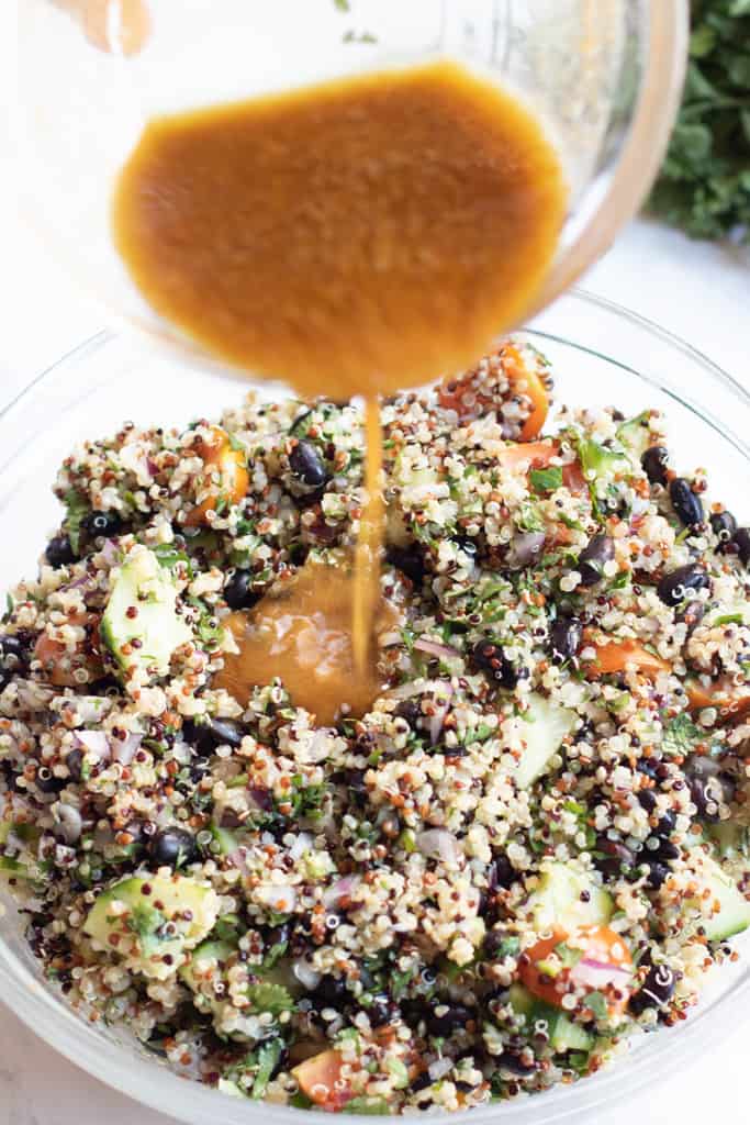 a bowl of quinoa salad with dressing being poured in