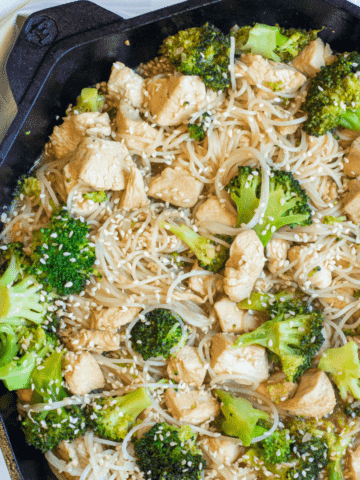 a cast iron with noodles, broccoli, and chicken with sesame seeds.