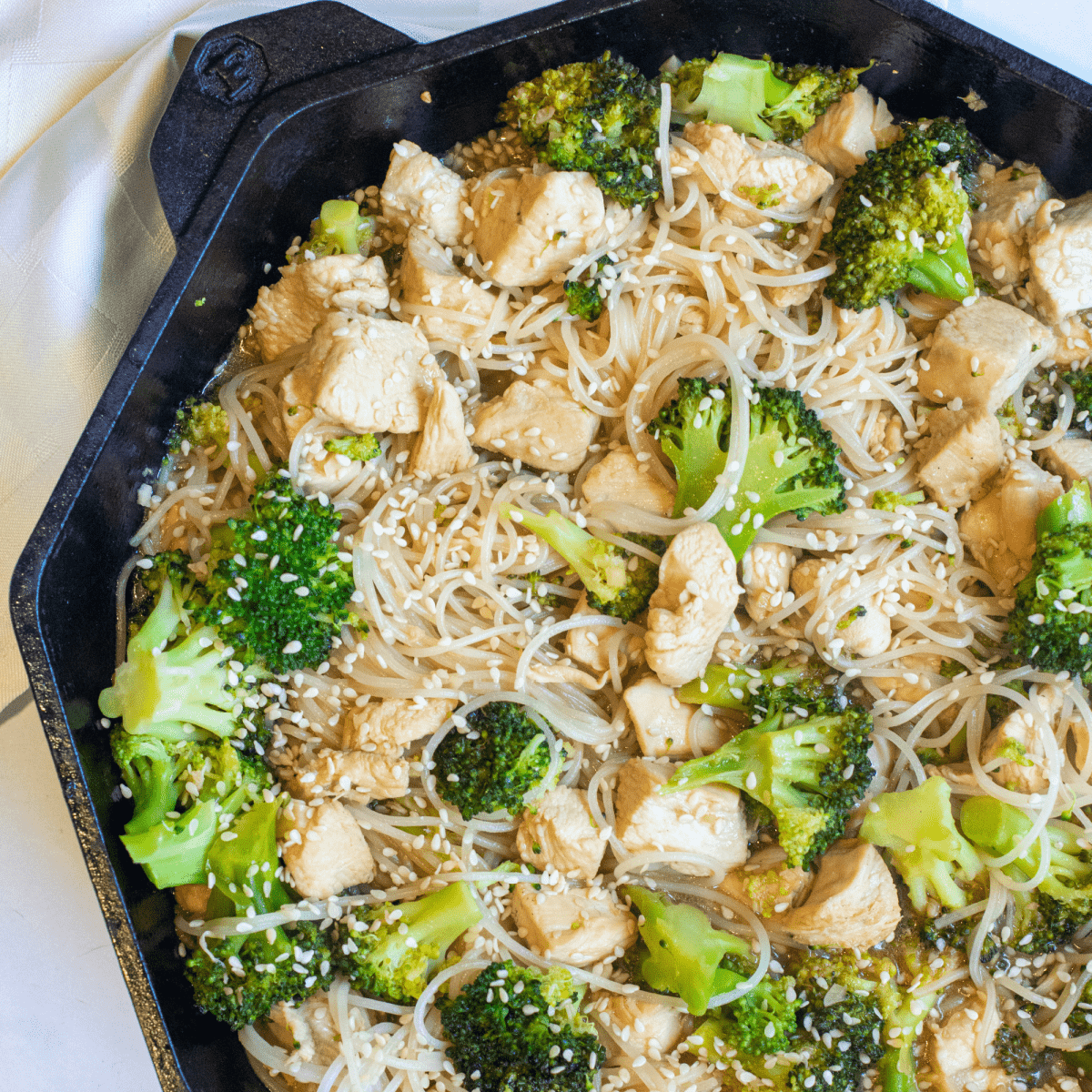 a cast iron with noodles, broccoli, and chicken with sesame seeds.