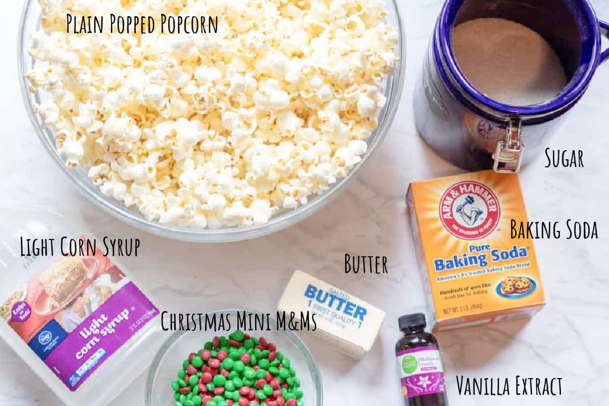 a large bowl of popcorn, sugar, light corn syrup, baking soda, butter, m&ms, and vanilla extract on a counter.