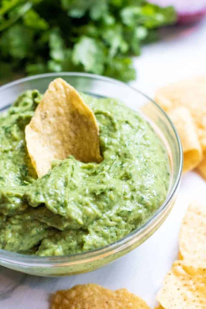 a bowl of guacamole with a chip in it.