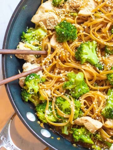 a pan with noodles, chicken, broccoli and chopsticks.