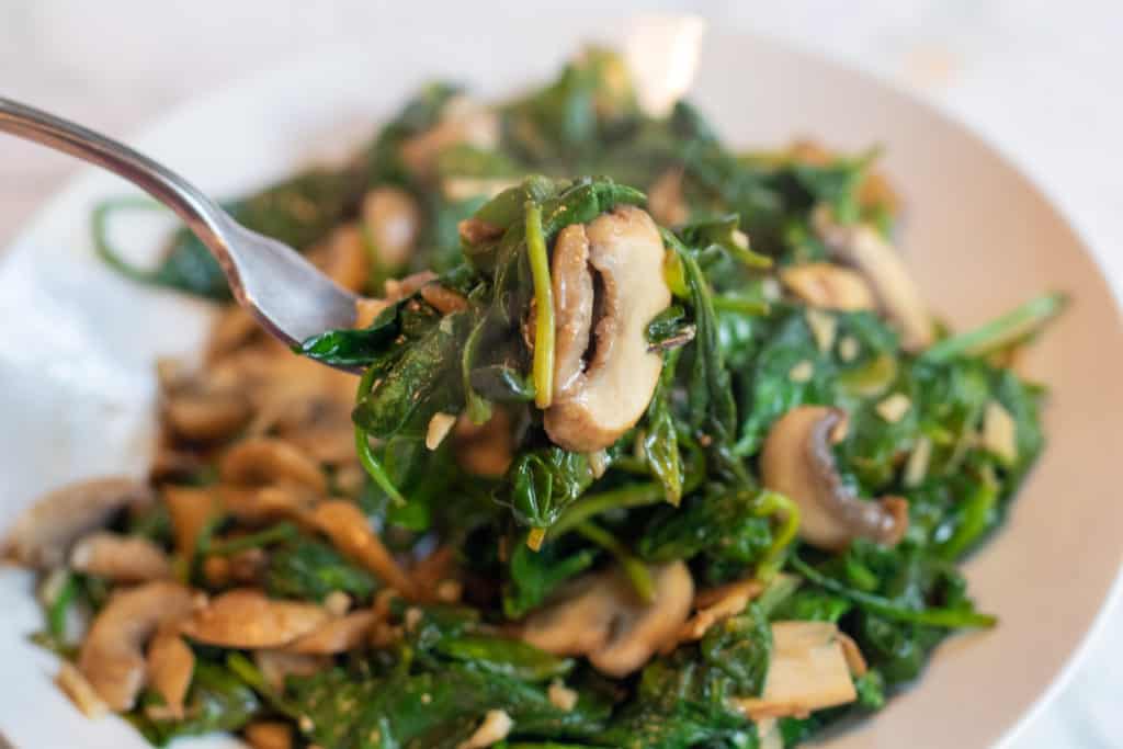 a bowl of sautéed spinach and mushrooms with a bite held up by a fork