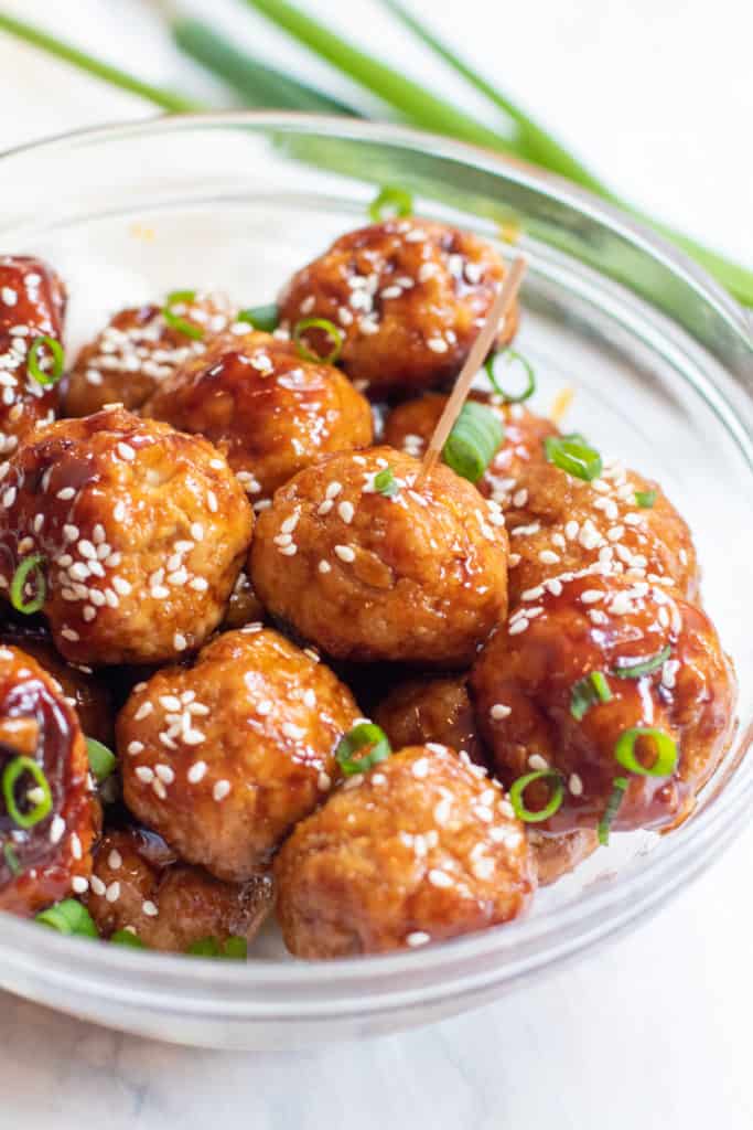 a bowl of meatballs topped with sesame seeds and one with a toothpick.