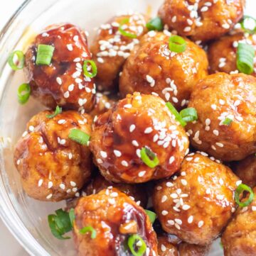 a bowl of meatballs topped with sesame seeds and green onions.