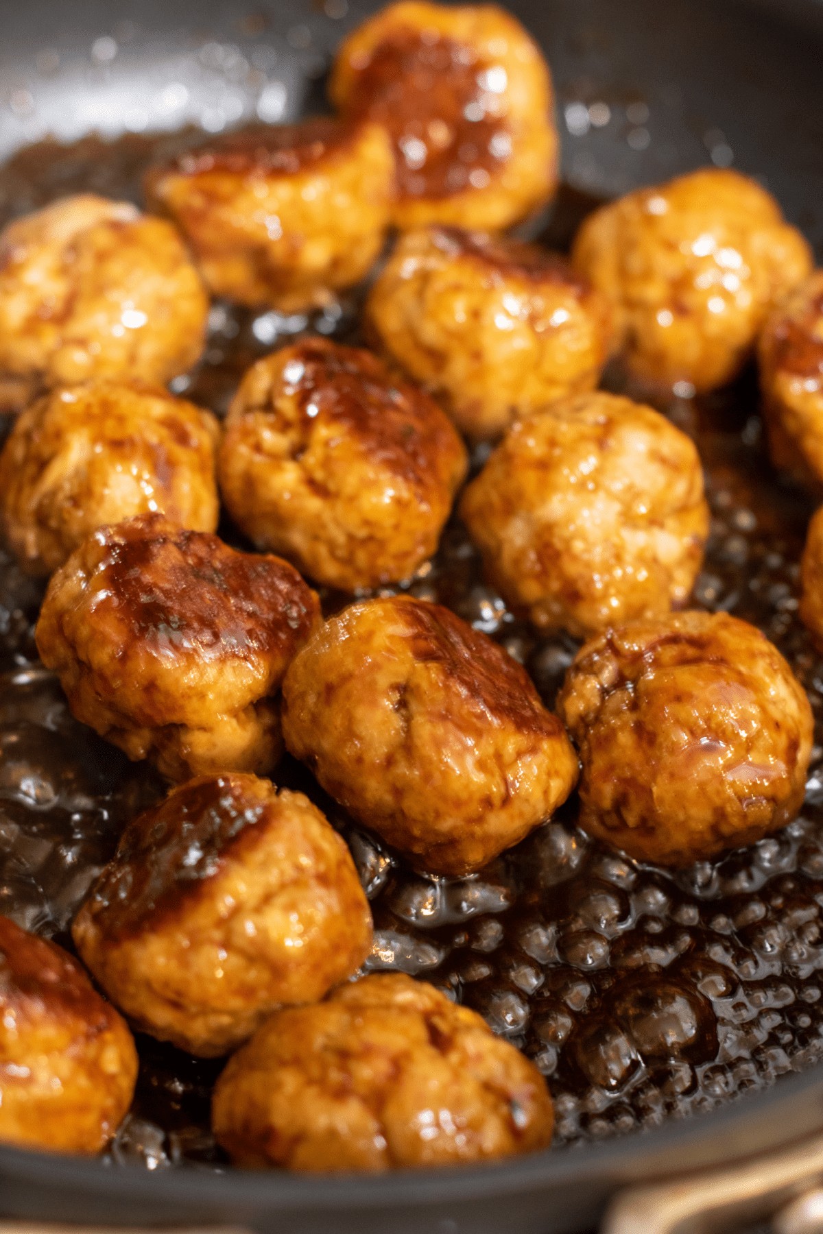 a pan with cooking meatballs in a sauce.