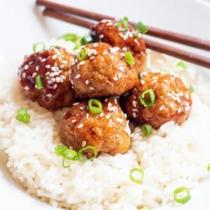 a bed of rice with meatballs topped with sesame seeds and green onions.