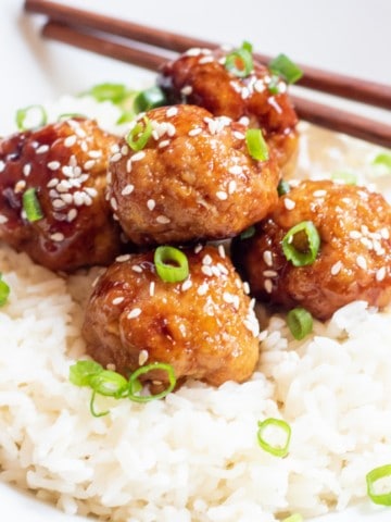 a bed of rice with meatballs topped with sesame seeds and green onions.