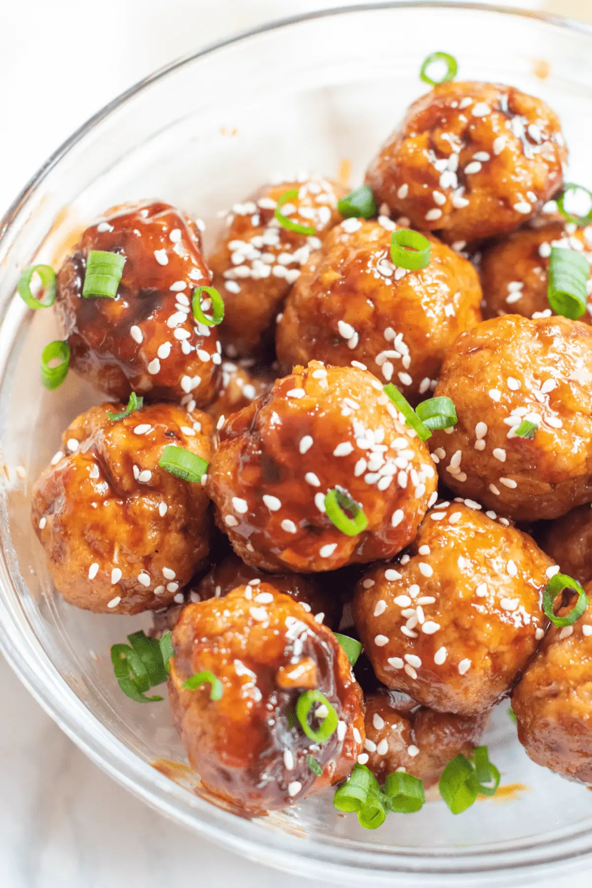 a bowl with meatballs topped with sesame seeds and green onions.