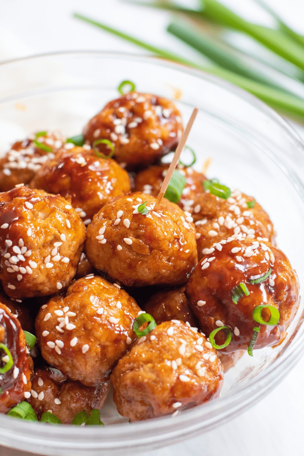a bowl with meatballs topped with sesame seeds and green onions.