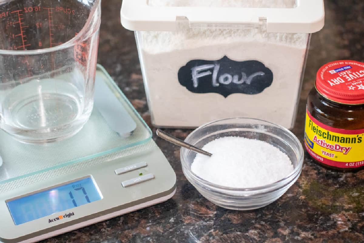 a kitchen scale with a pyrek of water, flour container, salt, and yeast.