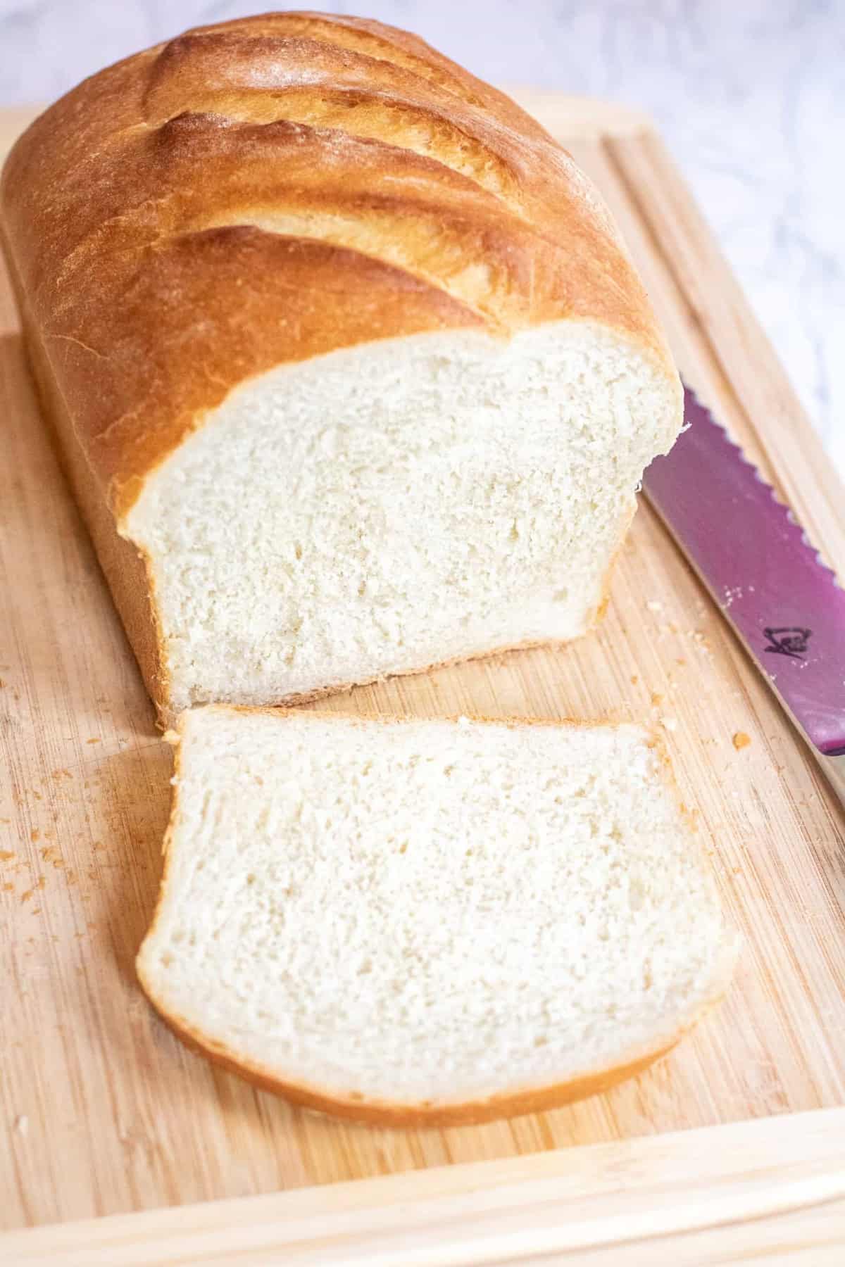 a loaf of white bread sliced on a cutting board.