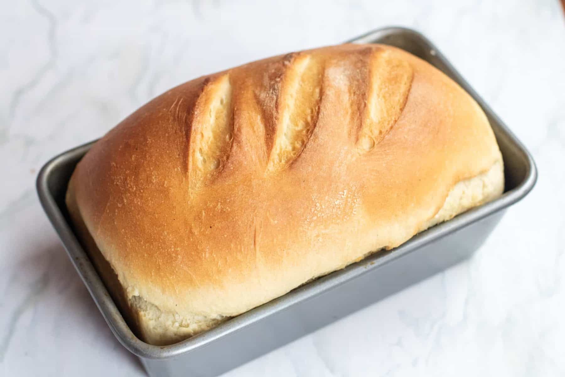 a baked loaf of white bread in a loaf pan.