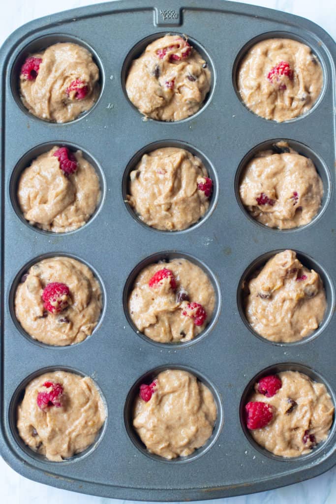 muffin tin filled with raspberry chocolate chip muffin dough