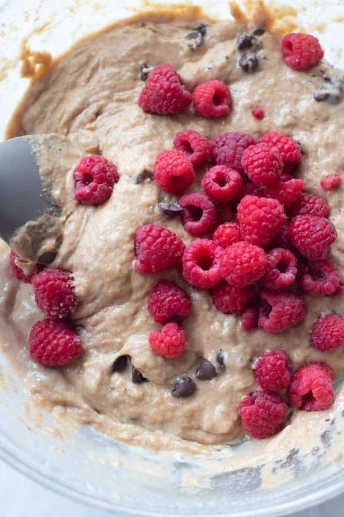 muffin batter in a bowl with chocolate chips and fresh raspberries