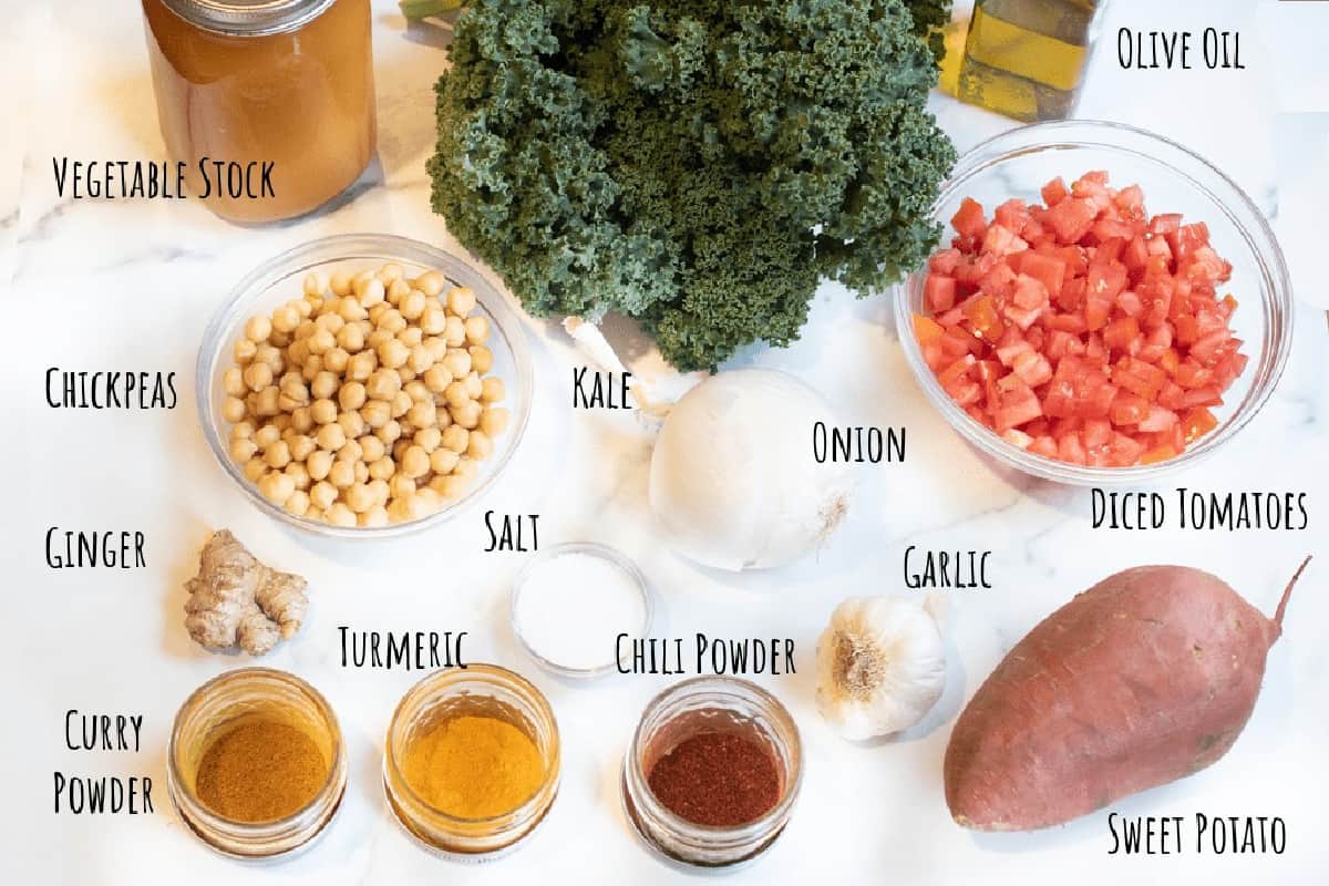 kale, stock, spices, chickpeas, garlic, ginger, diced tomatoes, oil, potato, onion on a counter.