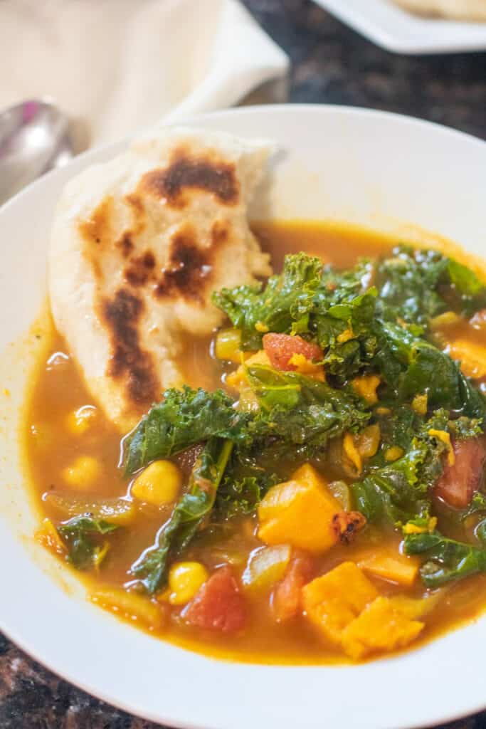 bowl of cook kale sweet potato soup with piece of naan.