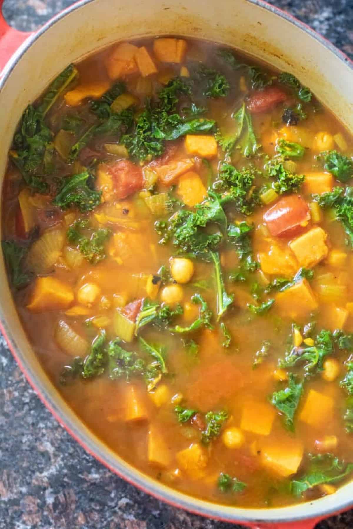 dutch oven of cooked chickpeas, sweet potato, kale soup with ladle.