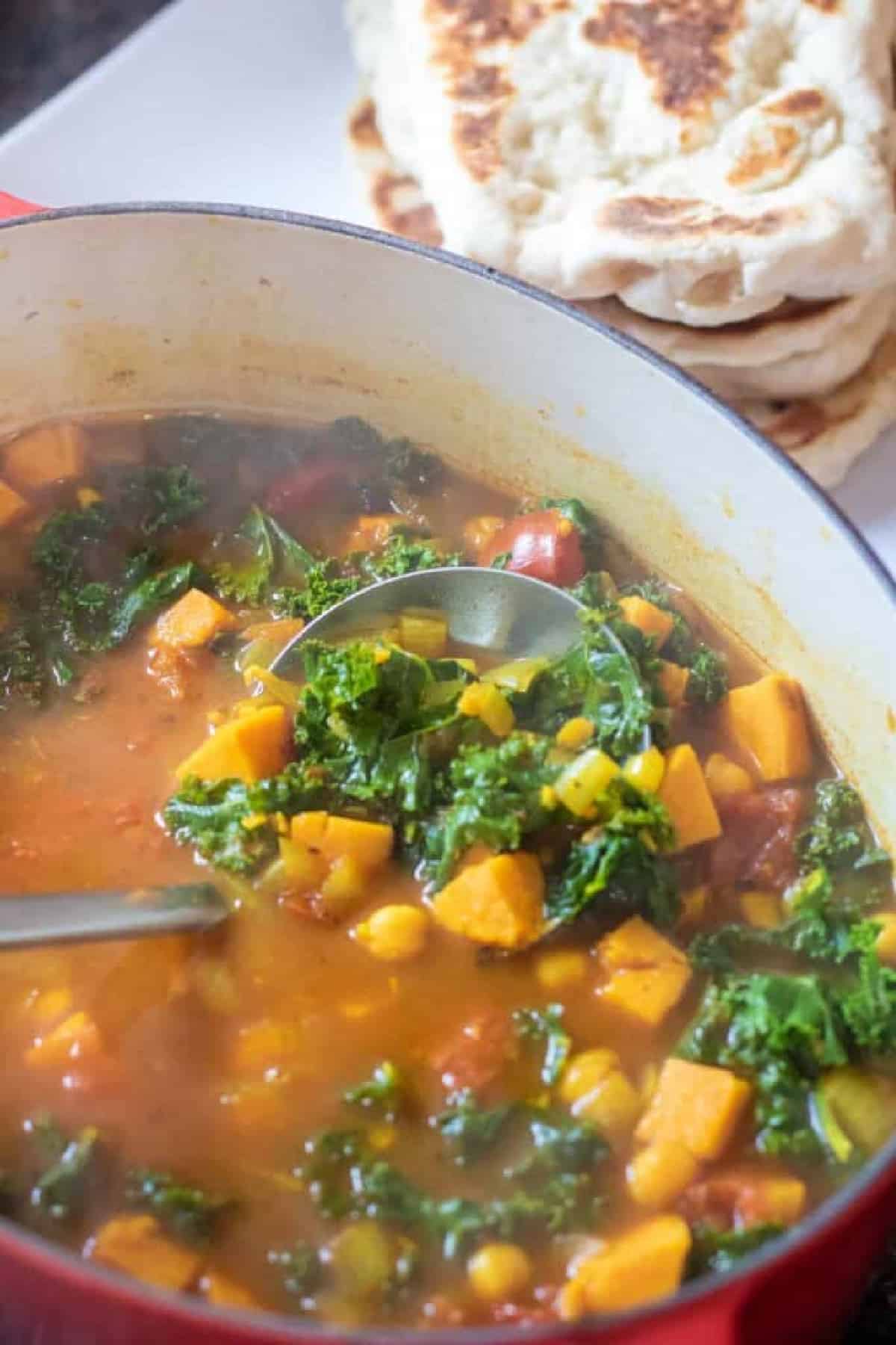 dutch oven of cooked chickpeas, sweet potato, kale soup with ladle.