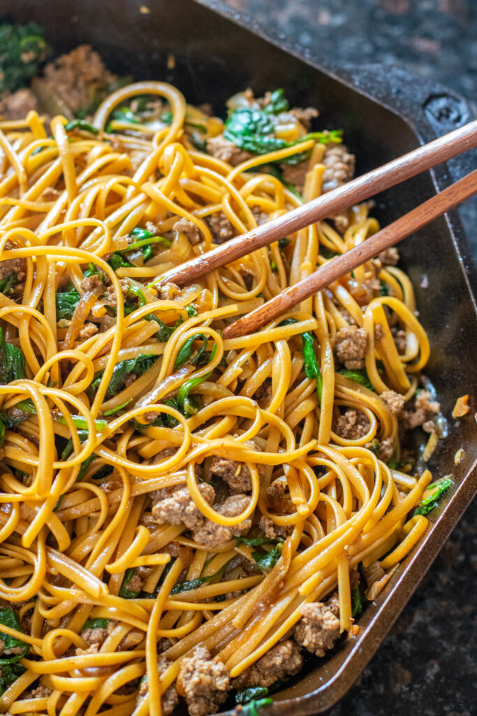 linguine noodles with spinach and ground beef in a cast iron with chopsticks