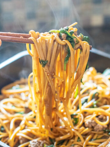 chopsticks holding cooked noodles with spinach and ground beef from cast iron.