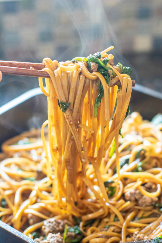 chopsticks holding cooked noodles with spinach and ground beef from cast iron.
