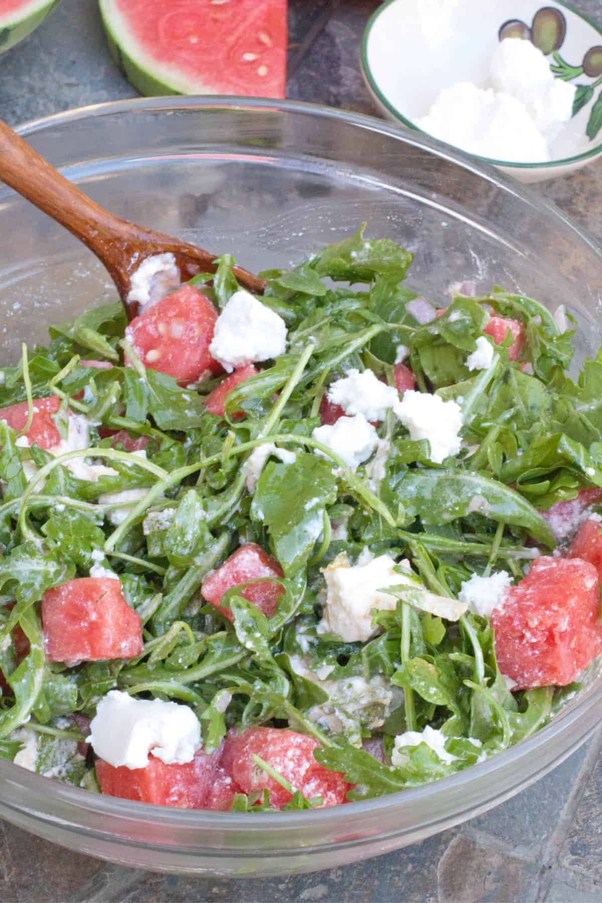 arugula watermelon feta salad in a large bowl with a wooden spoon.