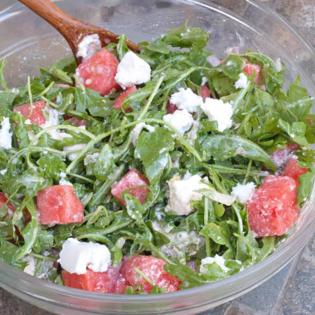 arugula watermelon feta salad in a large bowl with a wooden spoon.