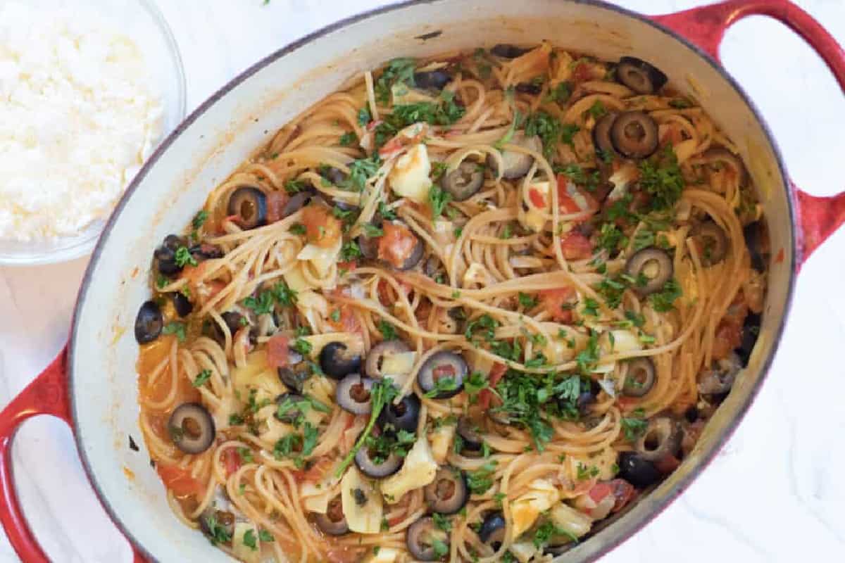 an overhead of a cooked pasta with olives, parsley, tomatoes, and artichokes.