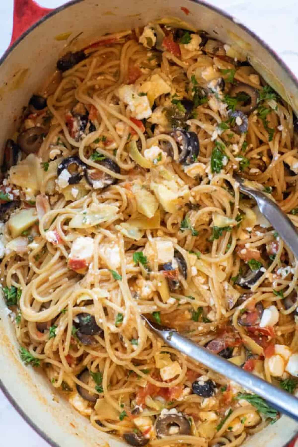 greek pasta in a pot with tongs topped with feta cheese.