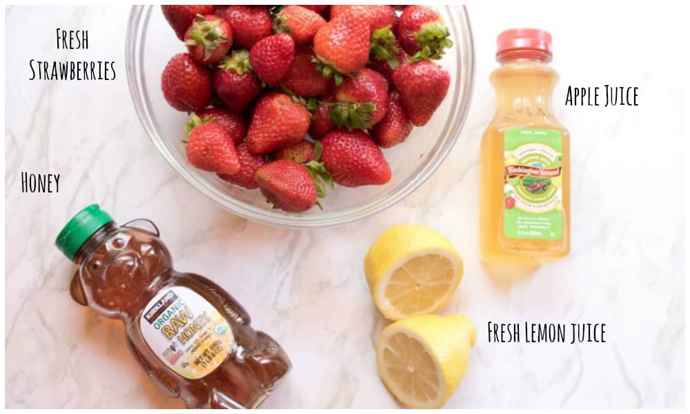 strawberries, honey, lemon, and apple juice on a counter.