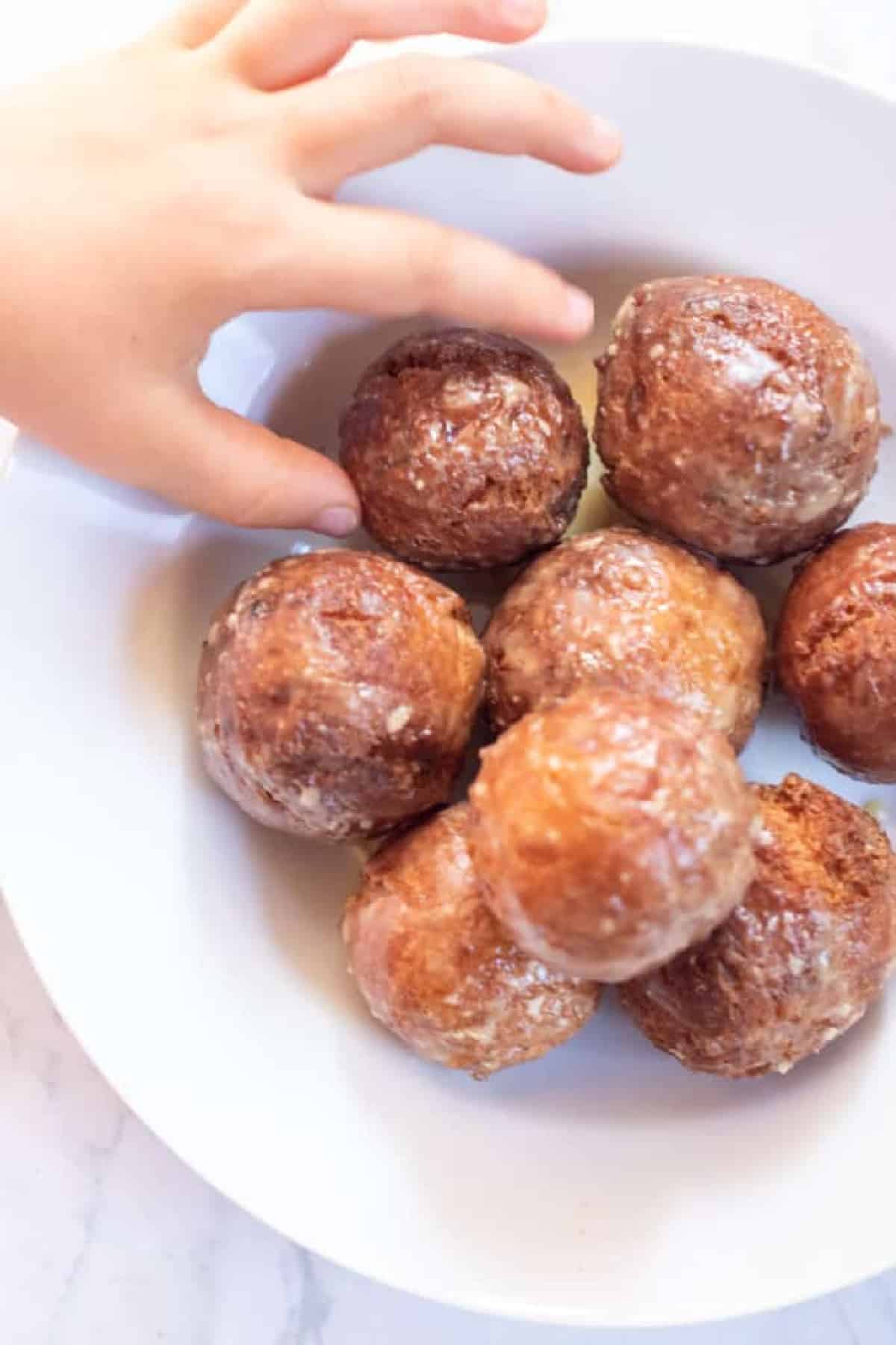 a bowl of glazed munchkins with a kids hand reaching for one.