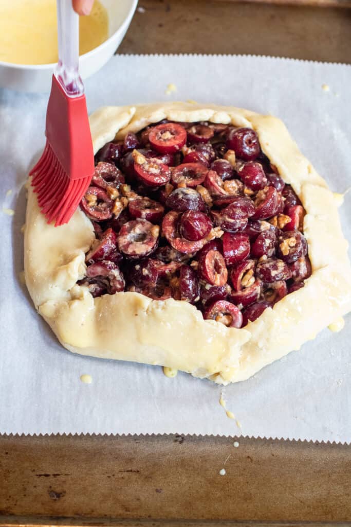 unbaked cherry galette being brushed for an egg wash