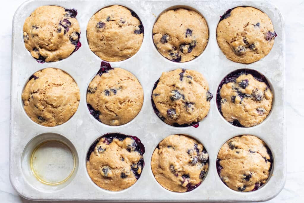 a muffin tin with baked blueberry muffins