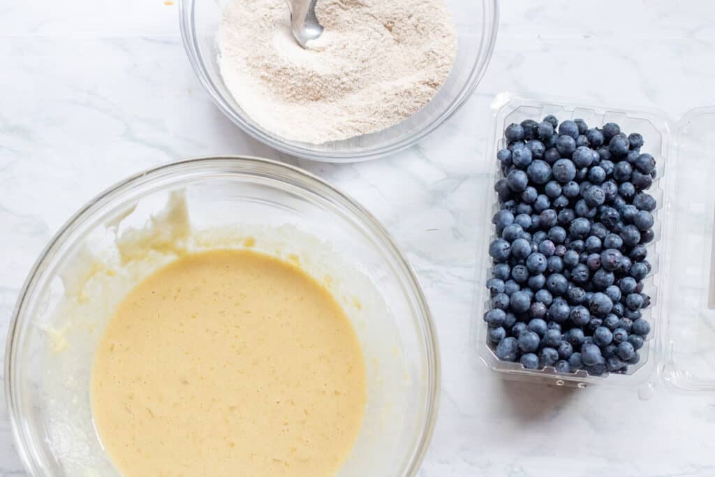 a bowl of batter and flour and blueberries on counter