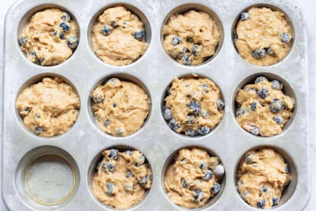 muffin tin filled with blueberry muffin dough.