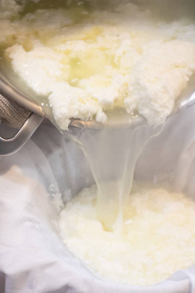 pouring curds and whey into a cheese cloth lined sieve 