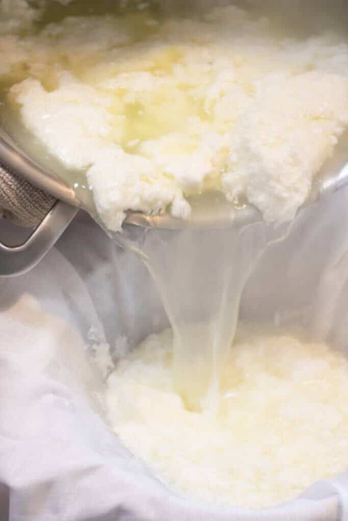 whey and curds being poured into a colander with a cheesecloth.