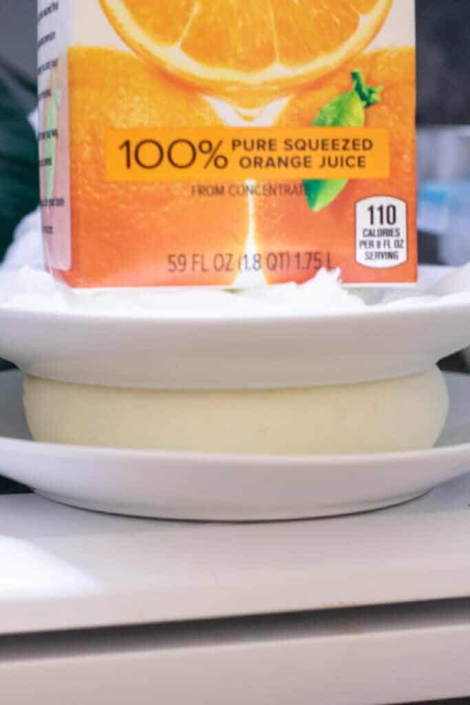 OJ on a plate pressing on cheese in a cheesecloth.