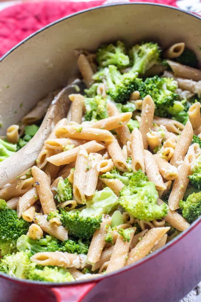 a pot of cooked penne and broccoli with a wooden spoon