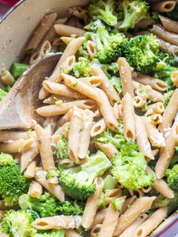 a pot of cooked penne and broccoli with a wooden spoon.