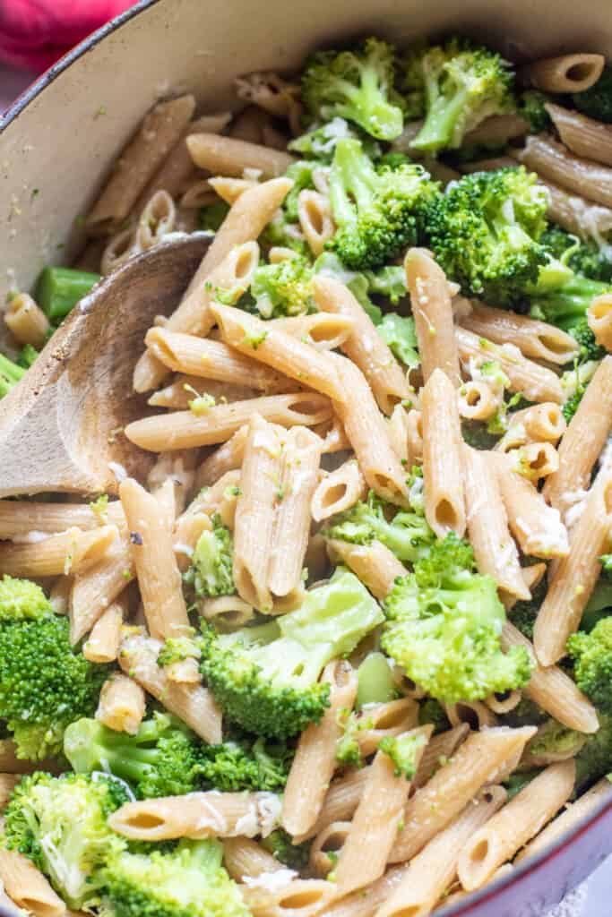 a pot of cooked penne and broccoli with a wooden spoon