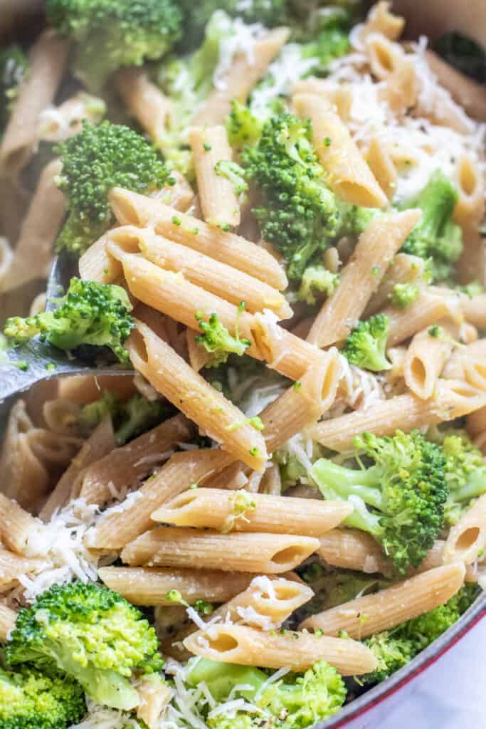 a pot of cooked penne, broccoli, mixed by a wooden spoon