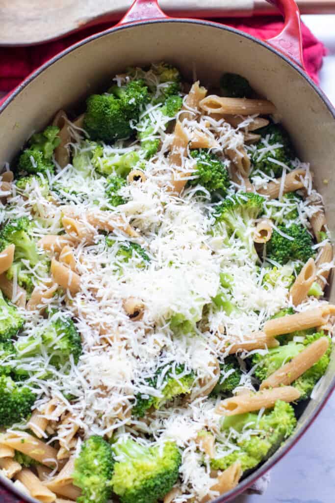 pot with cooked penne, broccoli, topped with shredded cheese