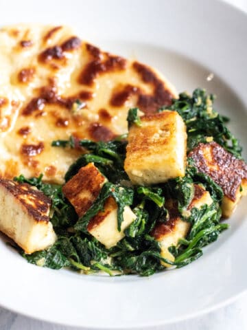 a plate with naan and paneer and spinach.